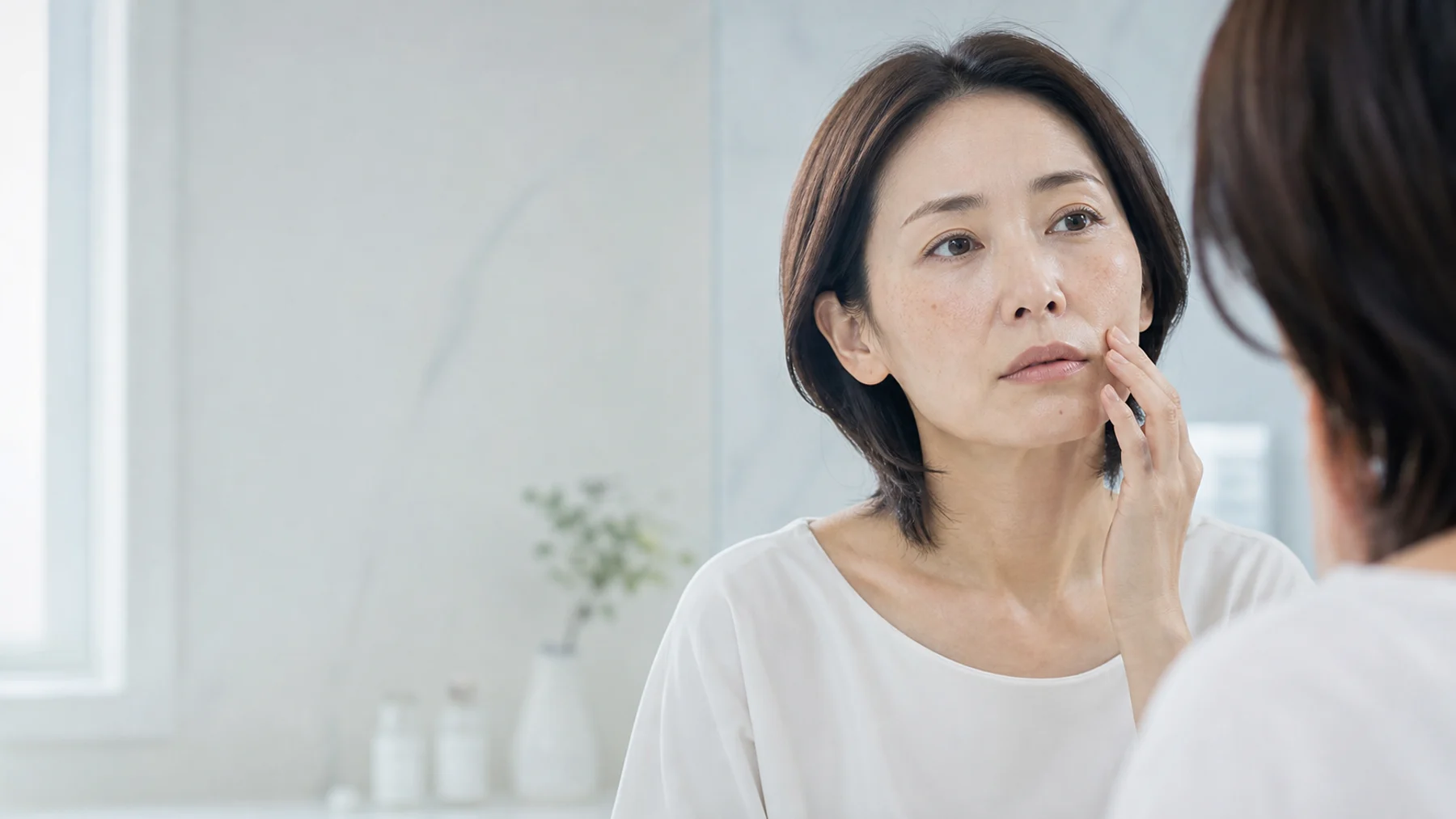 鏡で頬のシミを確認する女性の医療メディア向けイメージ