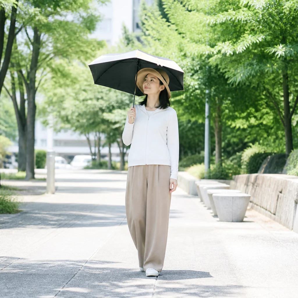 日差しを避けるために日傘をさし、帽子をかぶる女性の全身姿